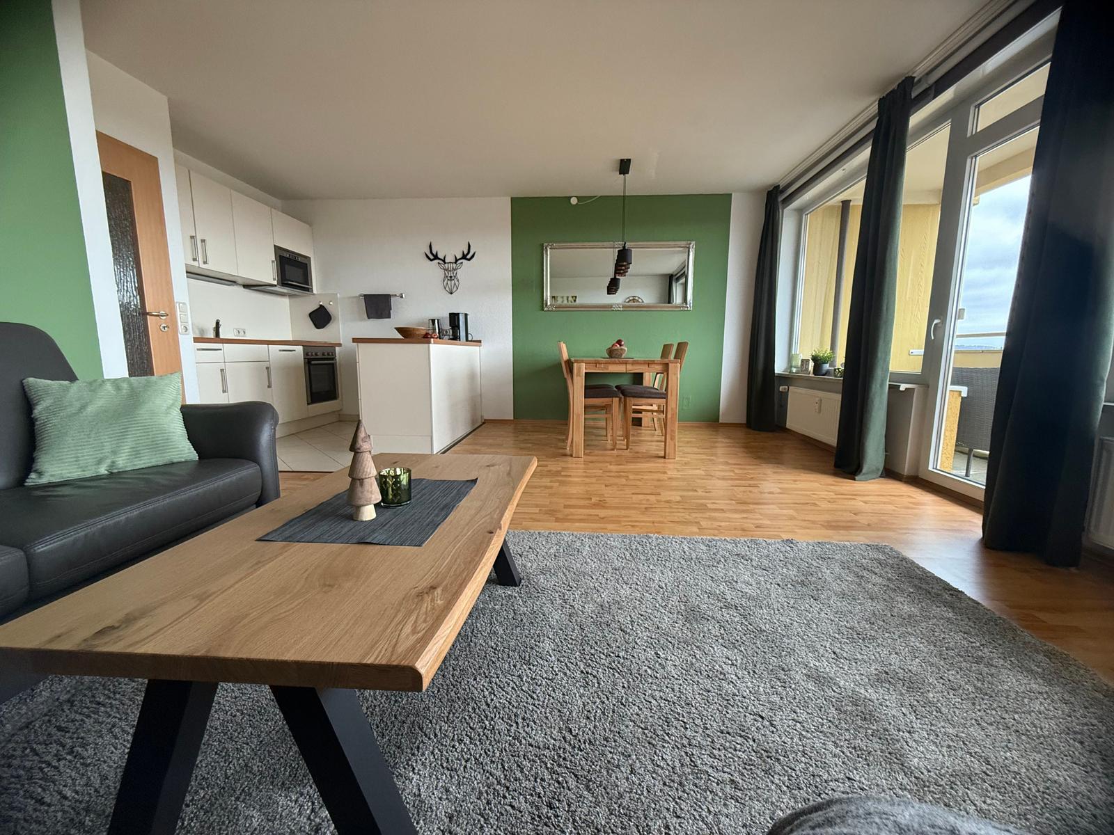 Wohnzimmer mit Küchenbereich und Essplatz. Holzfußboden und große Fenster.