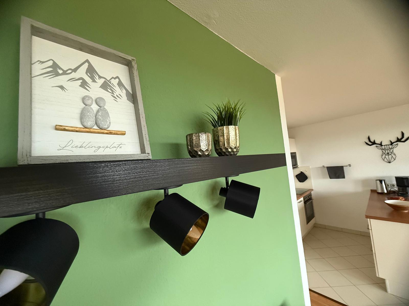 Grunder Wohnbereich mit grünem Wandbild und Küchenbereich im Hintergrund.