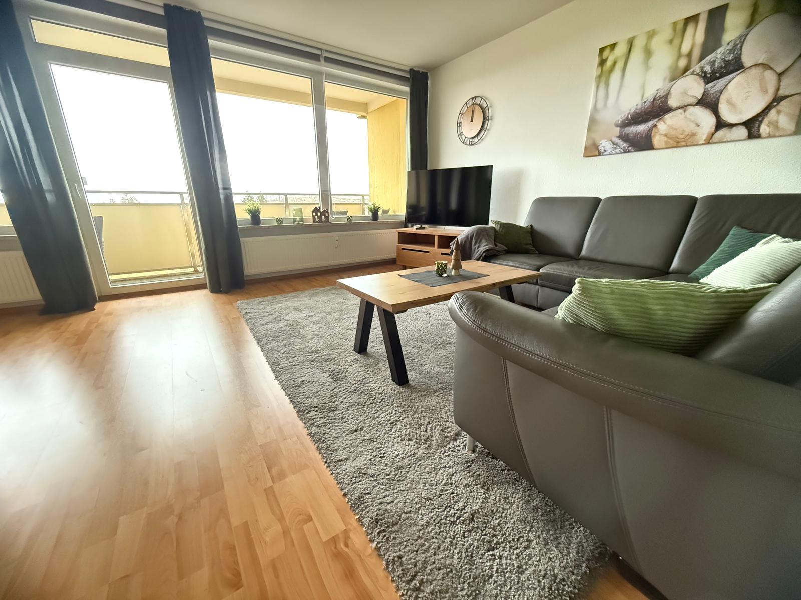 Wohnzimmer mit Sofa, Couchtisch und Balkon. Wandbild und Uhr sind sichtbar.