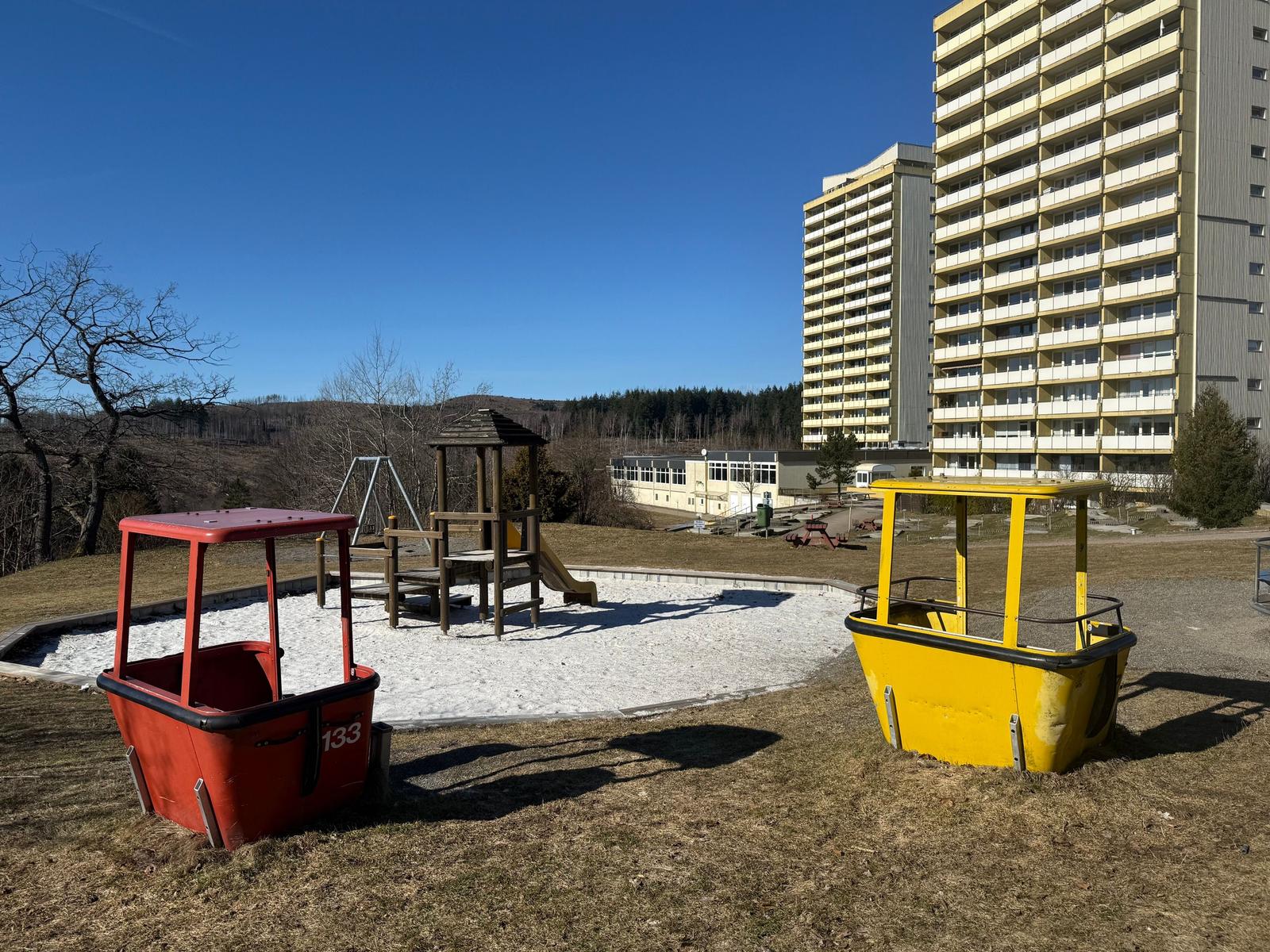 Kinderspielplatz mit Rutschbahn und zwei Fahrzeugen vor Hochhäusern.