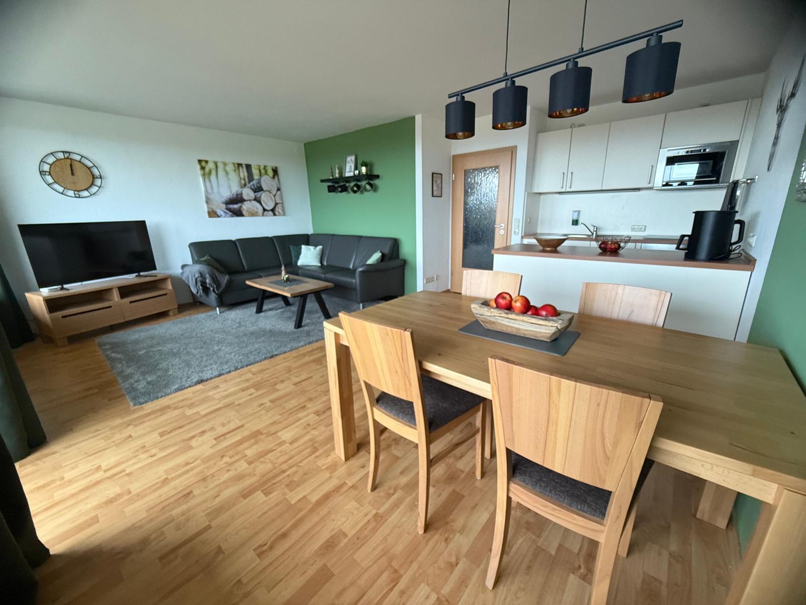 Wohn- und Essbereich mit Küche. Holztisch, Sofa, Fernseher und Küchenzeile.