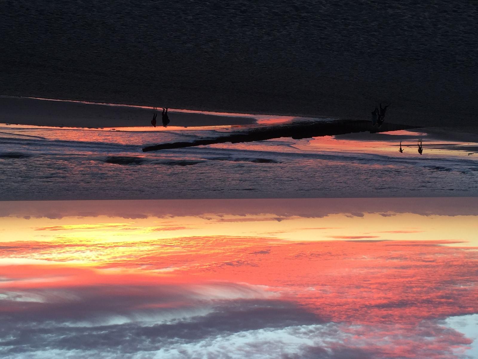 Sonnenuntergang am Strand mit Reflexion im Wasser und Silhouetten von Personen.