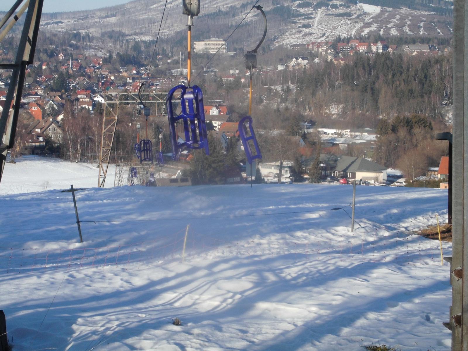Schneebedeckter Hang mit Seilbahn und Blick auf das Dorf.