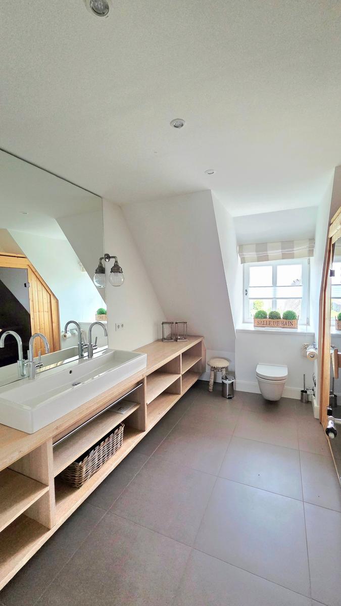 Badezimmer mit Waschbecken, Spiegel und Toilette unter Dachschrägen