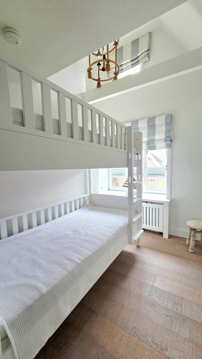 Ein Schlafzimmer mit Doppelstockbett, Holzboden und Fenster mit Rollladen.