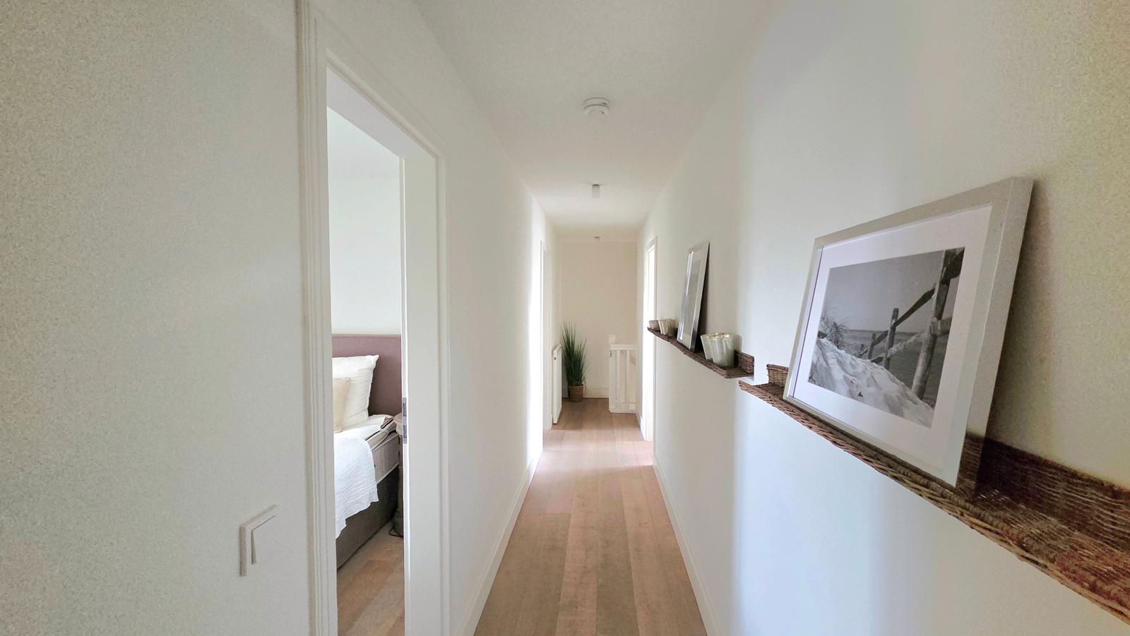 Flur mit Holzboden und Bildern an der Wand. Im Hintergrund ist ein Schlafzimmer sichtbar.