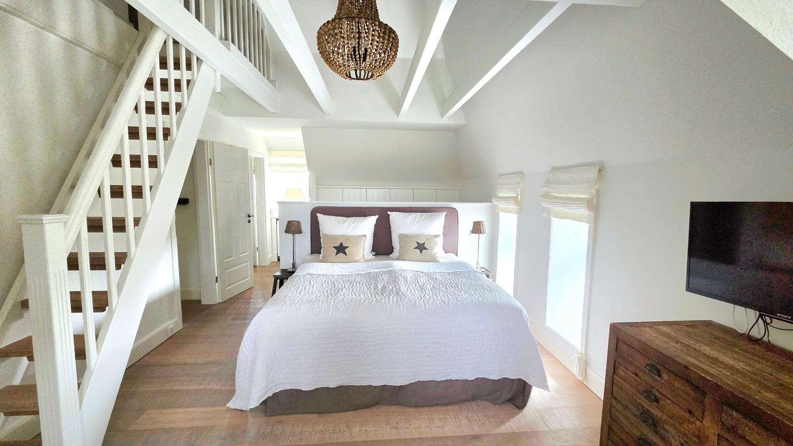 Schlafzimmer mit Dachschrägen, Bett, TV und Holztreppe.