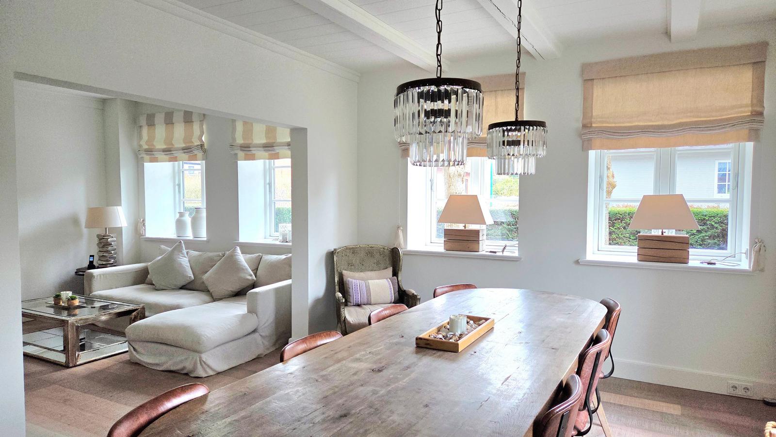 Essbereich mit langem Tisch und Stühlen, Wohnbereich mit Sofa und Fenstern.