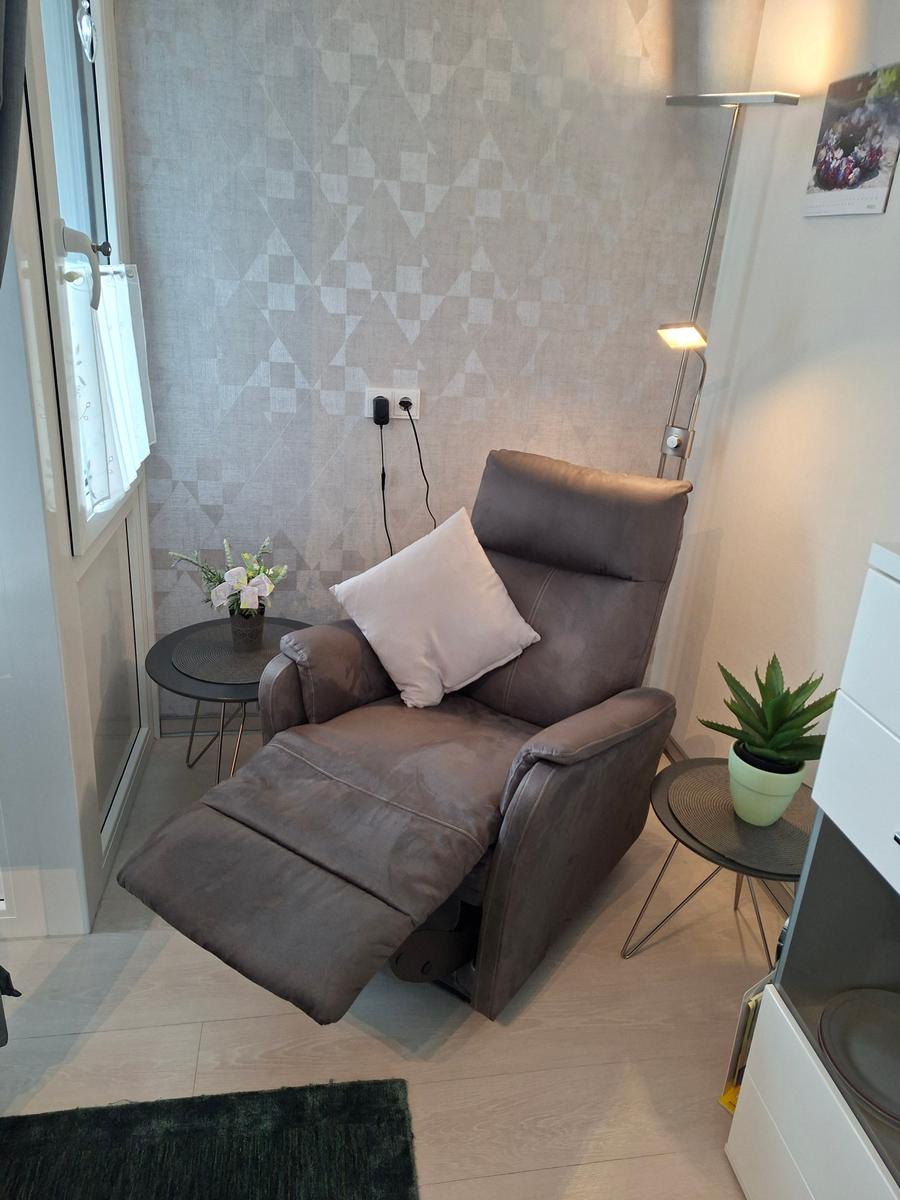 Ein braunes Relaxsessel mit Kissen, zwei runde Tische und eine Stehlampe.