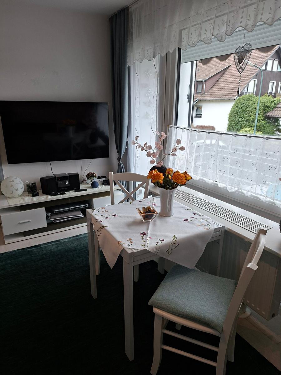 Esszimmer mit Tisch, Stühlen und TV. Fenster mit Vorhängen und Blumen.