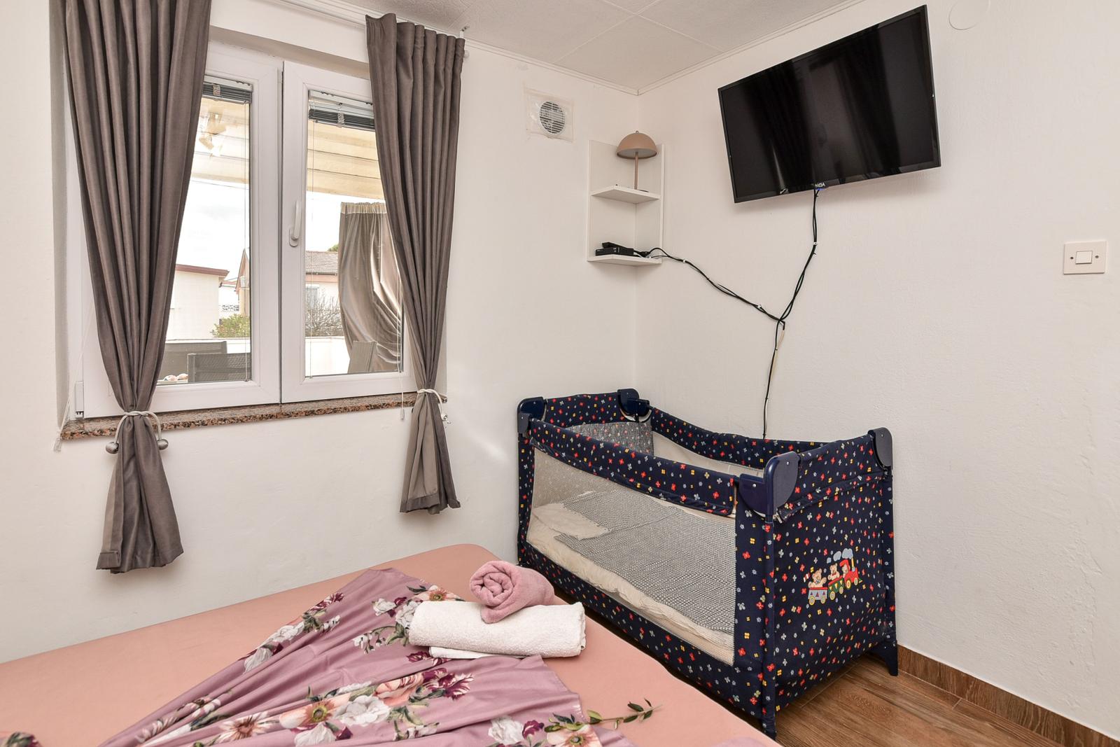 Zimmer mit Bett, Kinderbett, TV und Fenster mit Vorhängen.