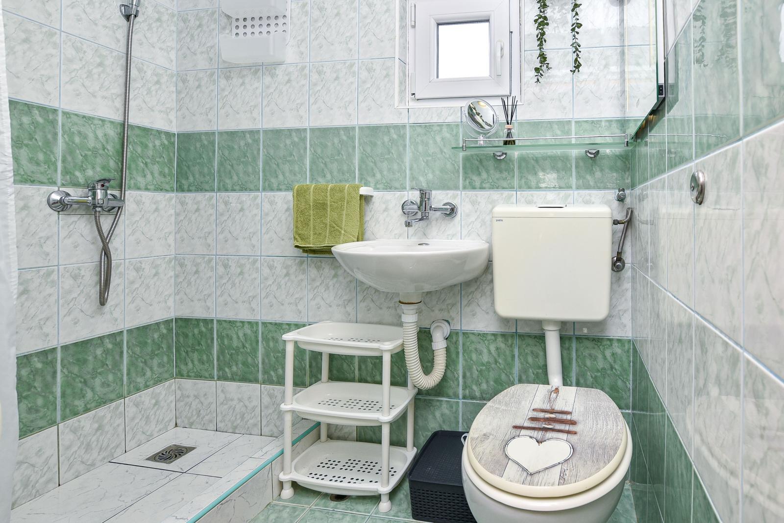 Badezimmer mit Dusche, Waschbecken und Toilette. Wandfliesen in Grün-Weiß.