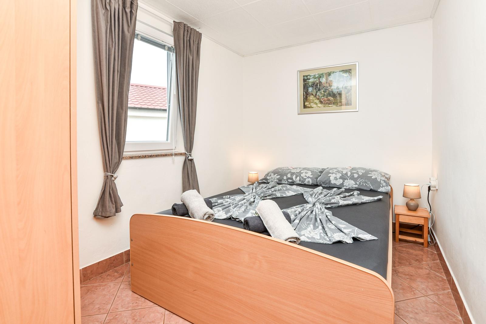 Schlafzimmer mit Bett, Nachttisch und Fenster mit Vorhängen.