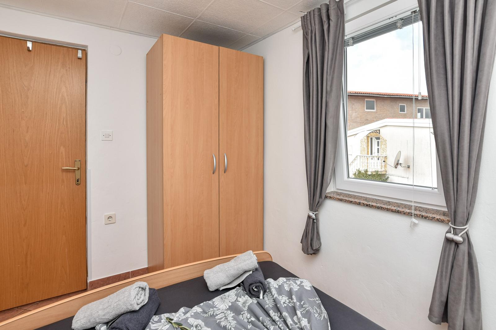 Schlafzimmer mit Bett, Kleiderschrank und Fenster mit Vorhängen.