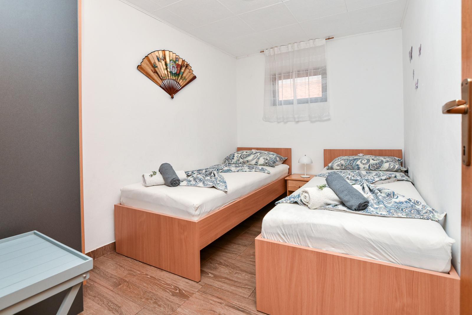 Zwei Einzelbetten mit Bettwäsche, Nachttisch und Fenster mit Vorhang.