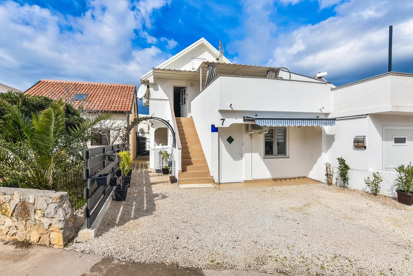 Weiße Villa mit Terrasse, Stufen und Gartenbereich unter blauem Himmel.