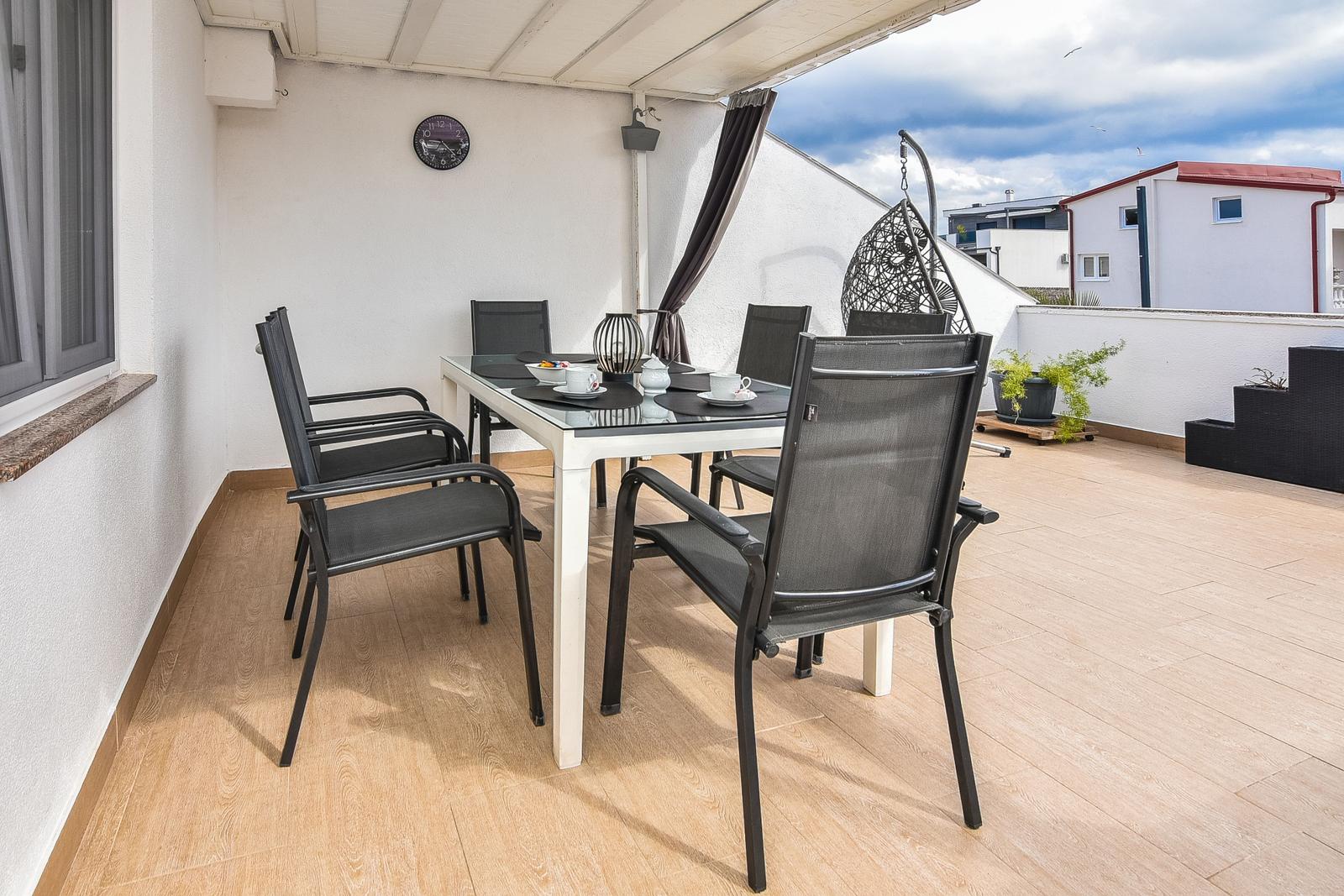 Terrasse mit Esstisch, Stühlen und Hängesessel. Holzfußboden und weißer Wand.