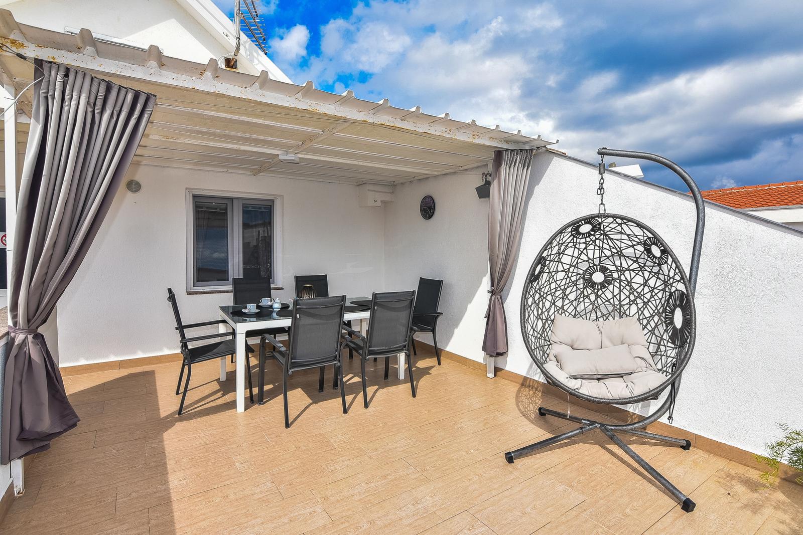 Terrasse mit Esstisch, Stühlen und Hängesessel unter Dach.