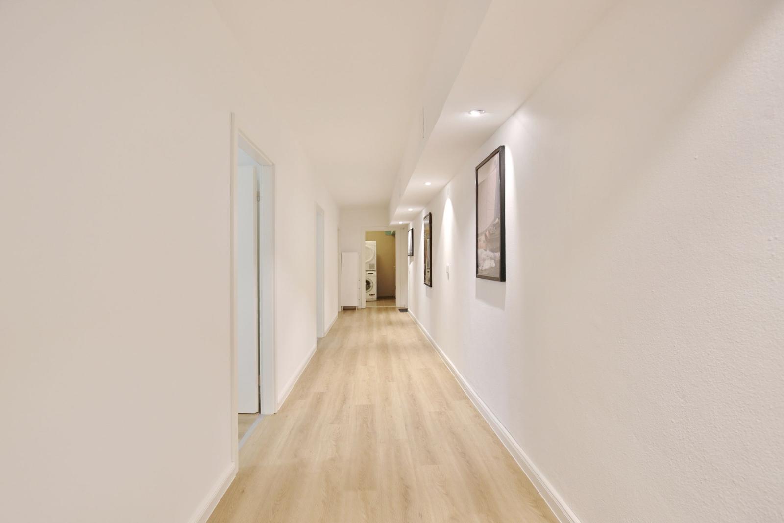 Flur mit hellen Wänden, Holzboden und Bildern an der Wand.