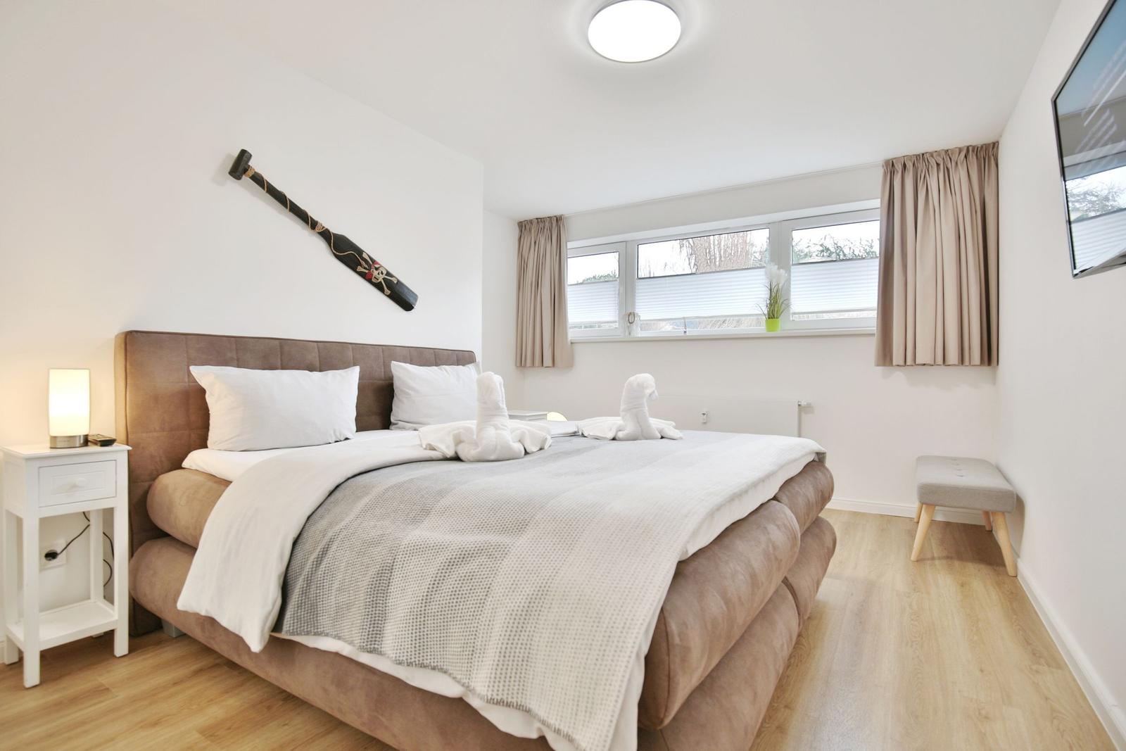 Schlafzimmer mit Bett, Nachttisch, Fenster und Wanddekoration.