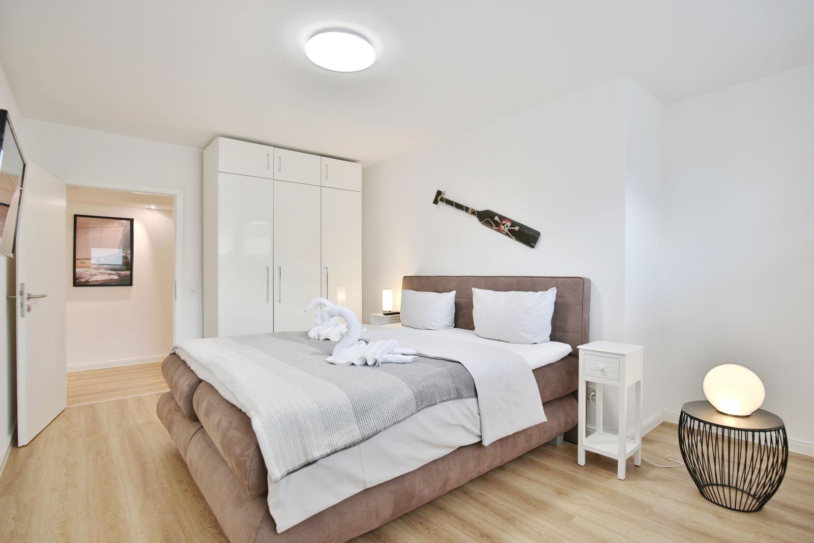Schlafzimmer mit Bett, Kleiderschrank und Nachttisch. Wanddekoration und Bodenbelag sichtbar.