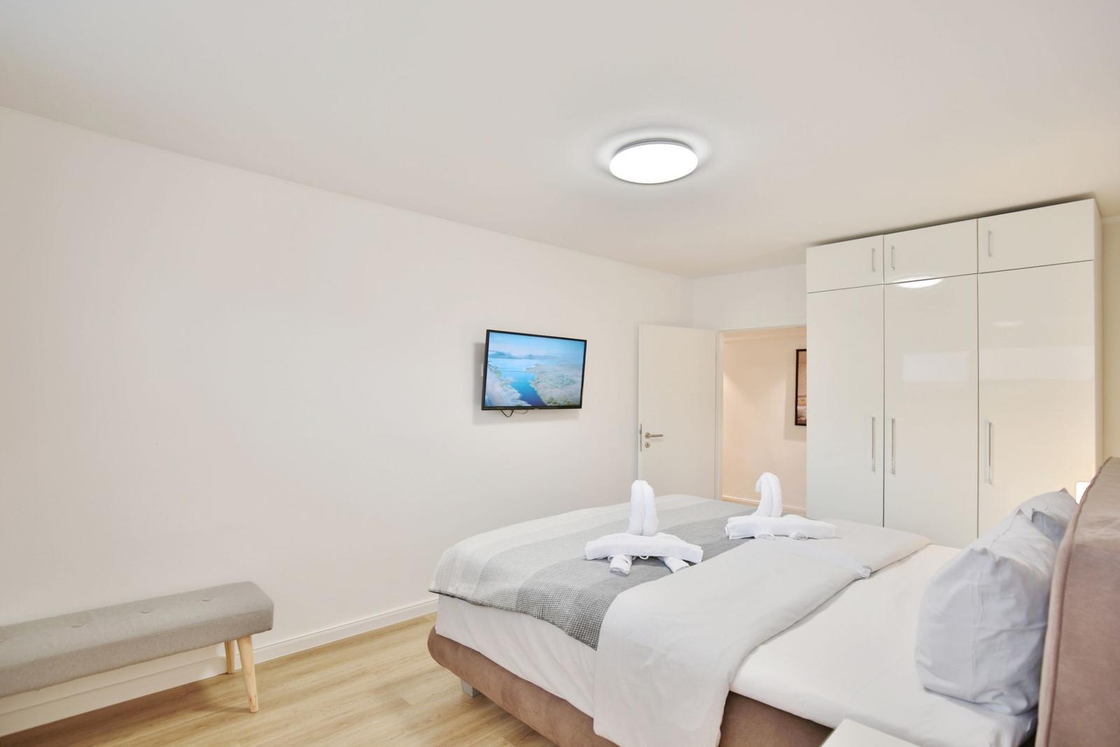 Schlafzimmer mit Bett, Kleiderschrank und Wandfernseher.