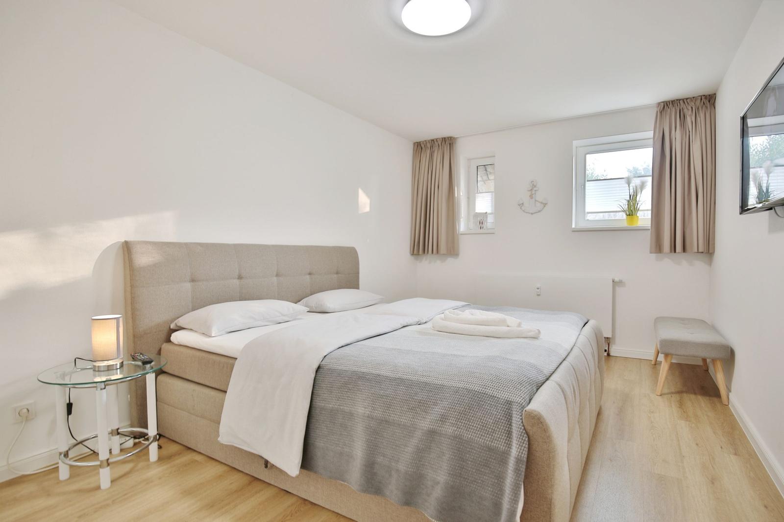 Schlafzimmer mit Doppelbett, Fenster, TV und Nachttisch.