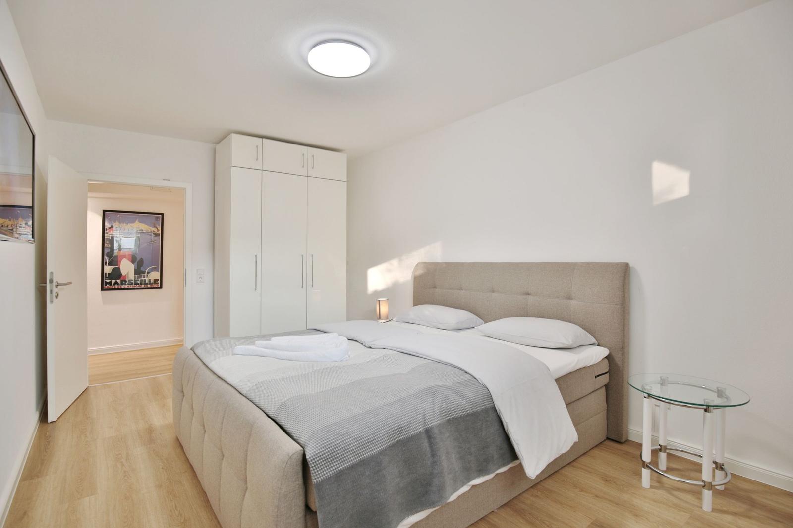 Schlafzimmer mit Bett, Kleiderschrank und Glasnachttisch.