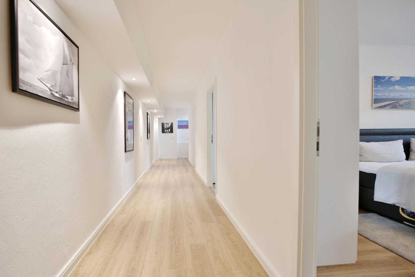 Flur mit Holzboden und Wandbildern, Blick in Schlafzimmer mit Bett.