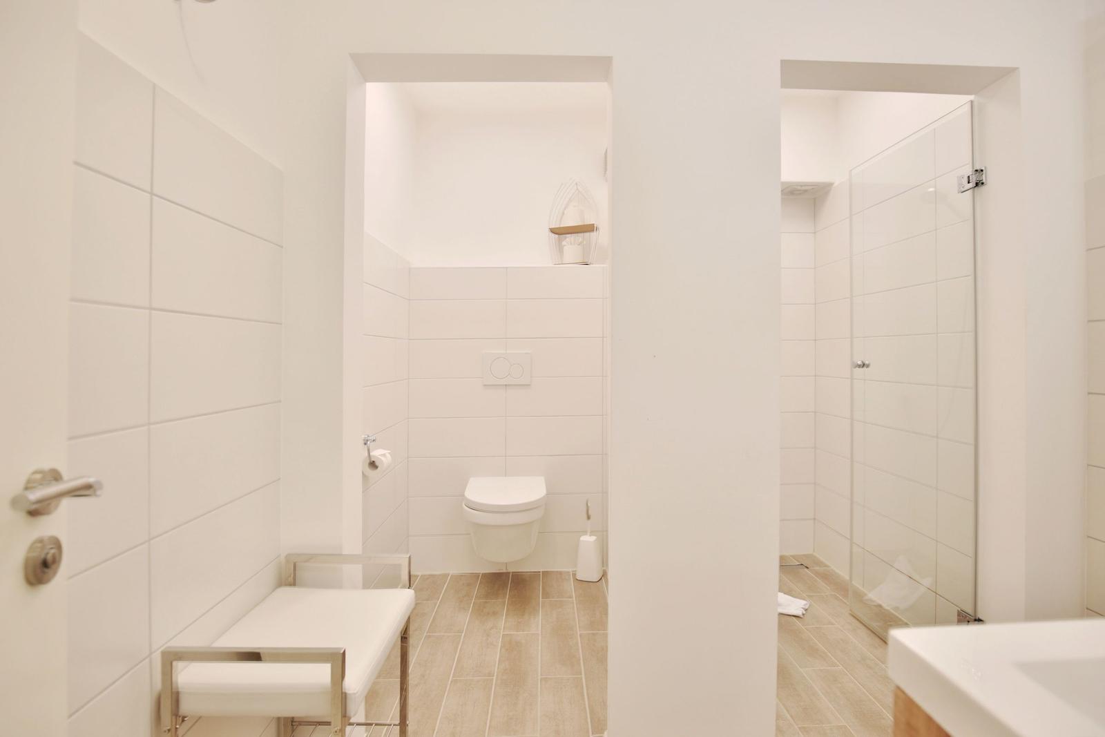 Bad mit Toilette, Dusche und Waschtisch. Fliesenwand und Holzboden.
