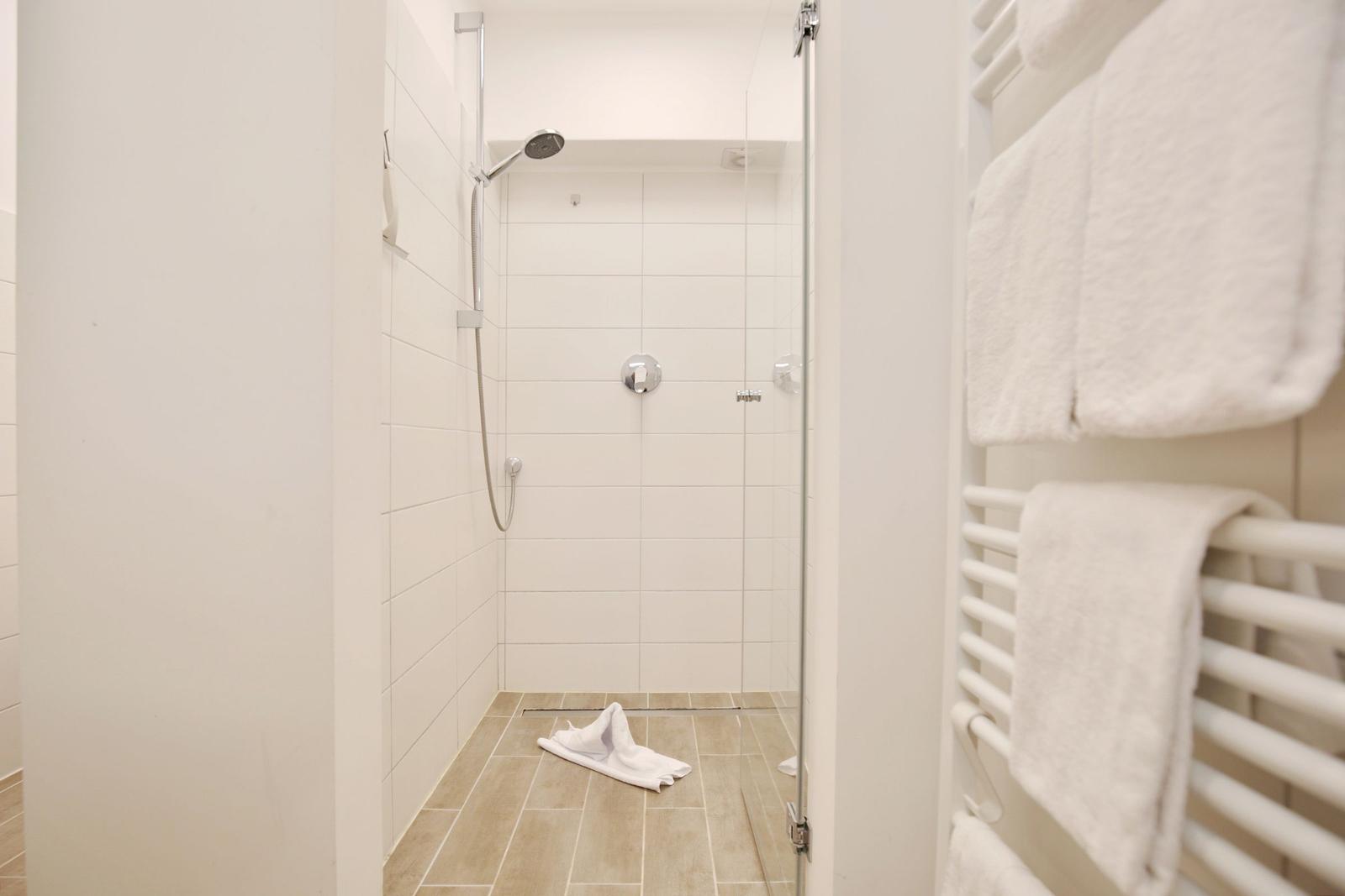 Dusche mit Glaswand, weißen Fliesen und Handtuchhalter