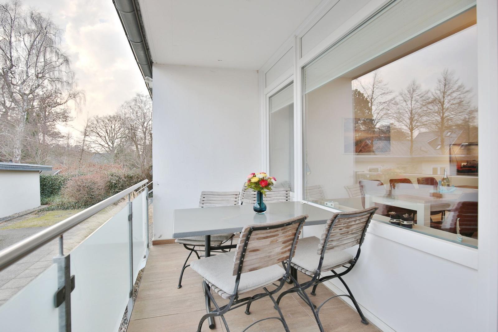Terrasse mit Tisch und Stühlen, Blick auf Bäume und Garten.