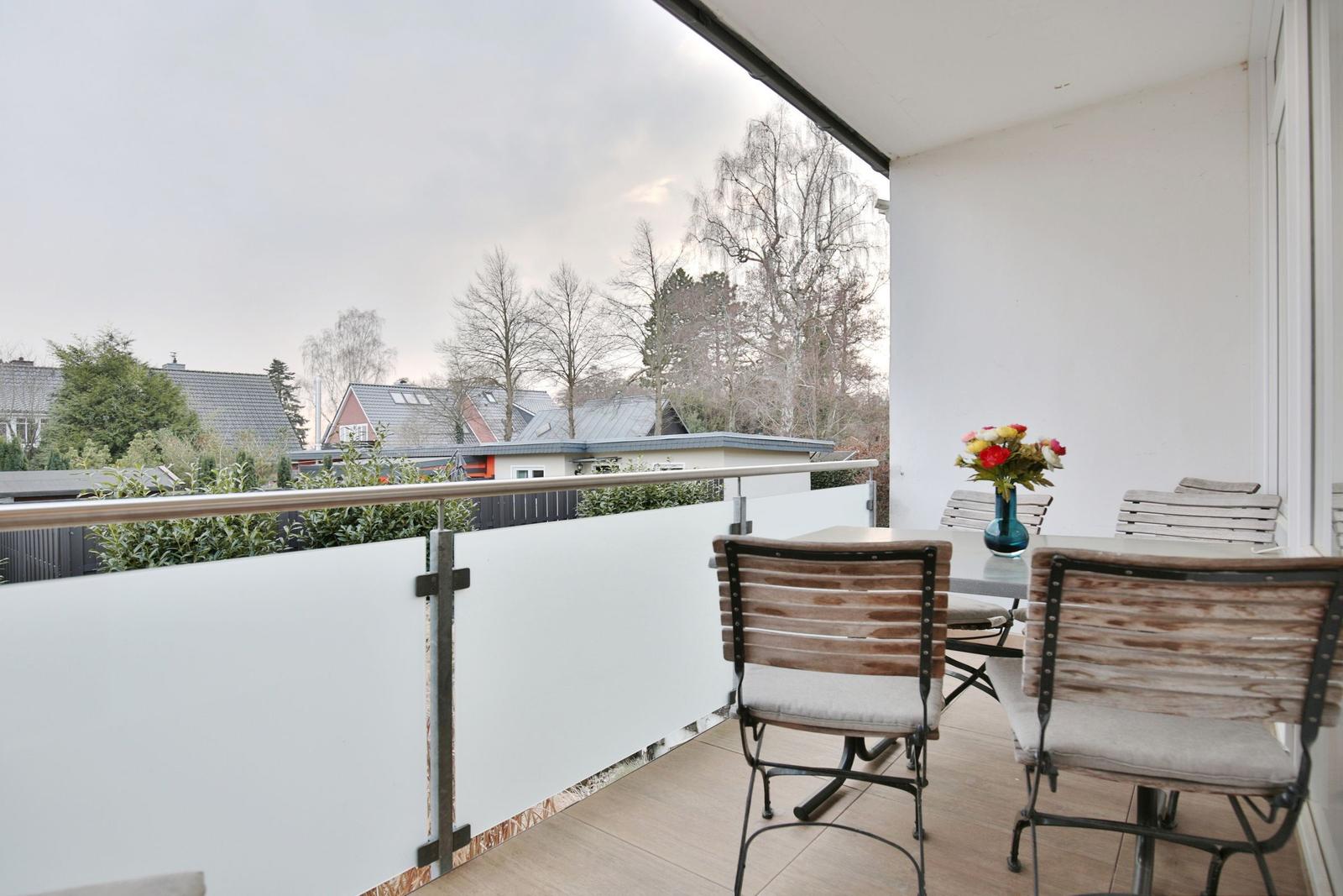 Terrasse mit Tisch, Stühlen und Blumenarrangement. Blick auf Bäume und Häuser.