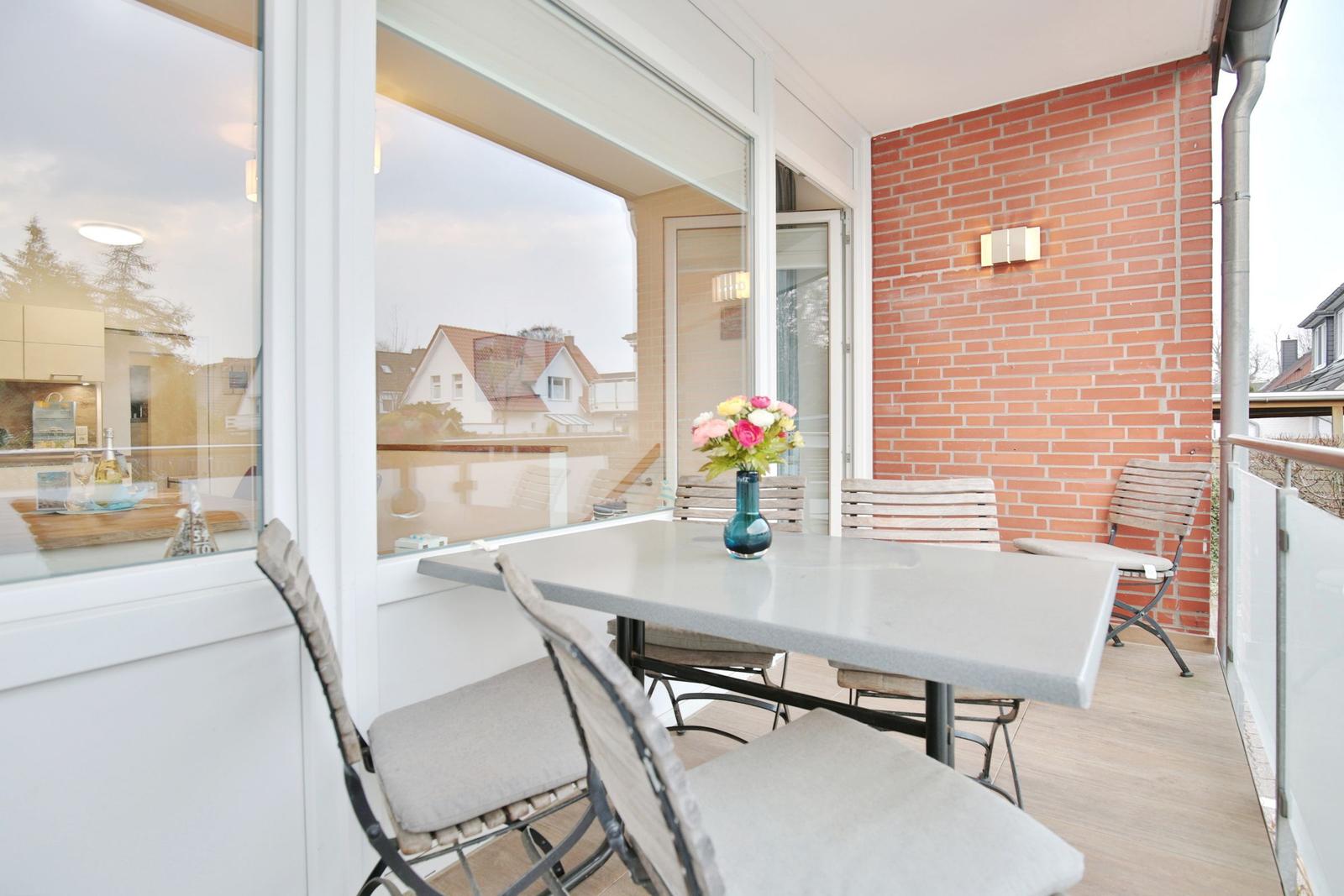 Terrasse mit Tisch, Stühlen und Blumenarrangement. Roter Backsteinwand und Glasfront.