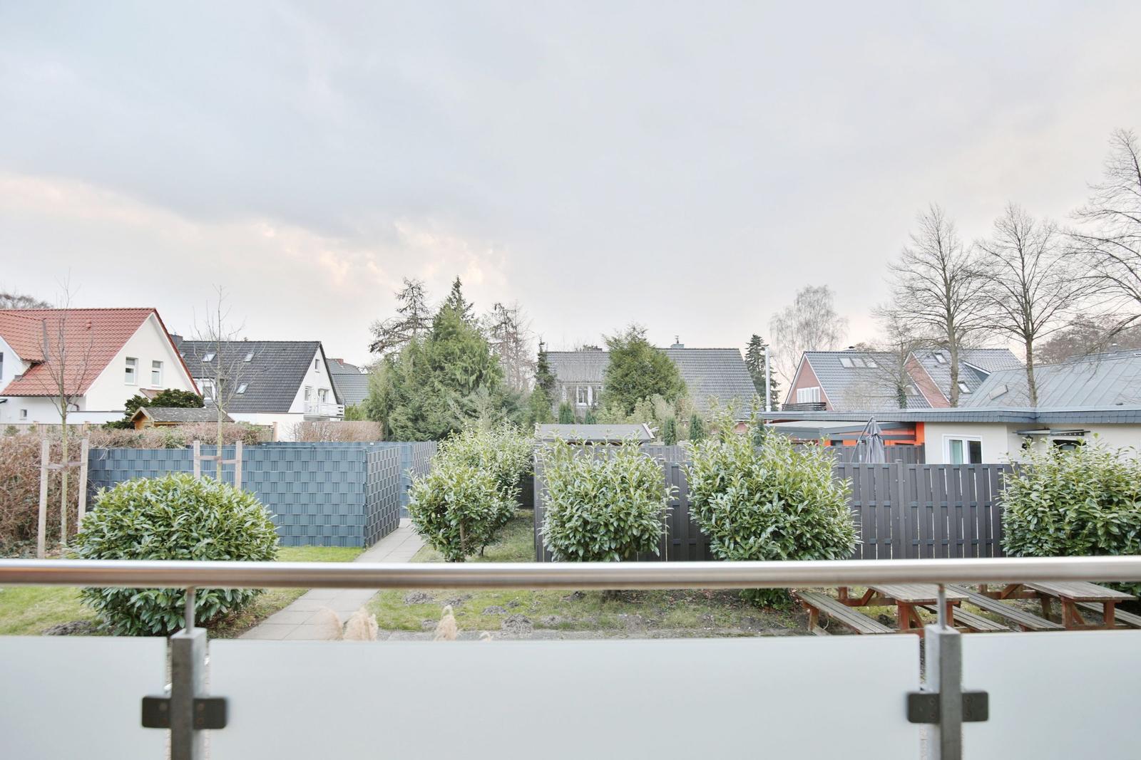 Blick von Balkon auf gepflegten Garten mit Bäumen und Nachbarhäusern