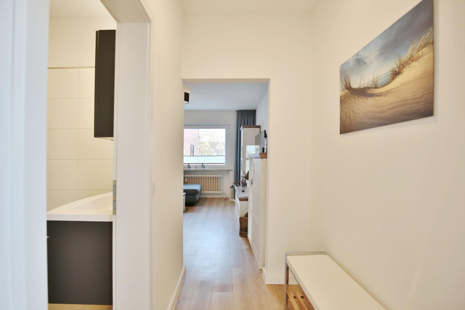 Flur mit Badezimmer und Blick in Wohnbereich mit Fenster.
