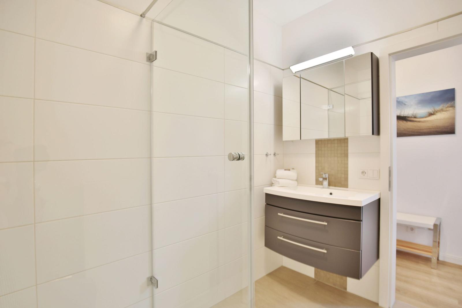 Badezimmer mit Dusche, Waschbecken und Spiegelschrank.