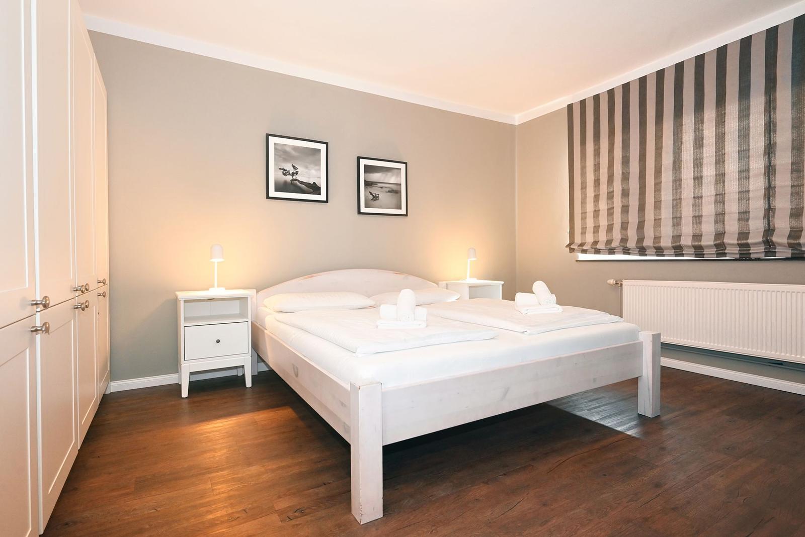 Schlafzimmer mit Bett, Nachttischen und Gardinen.