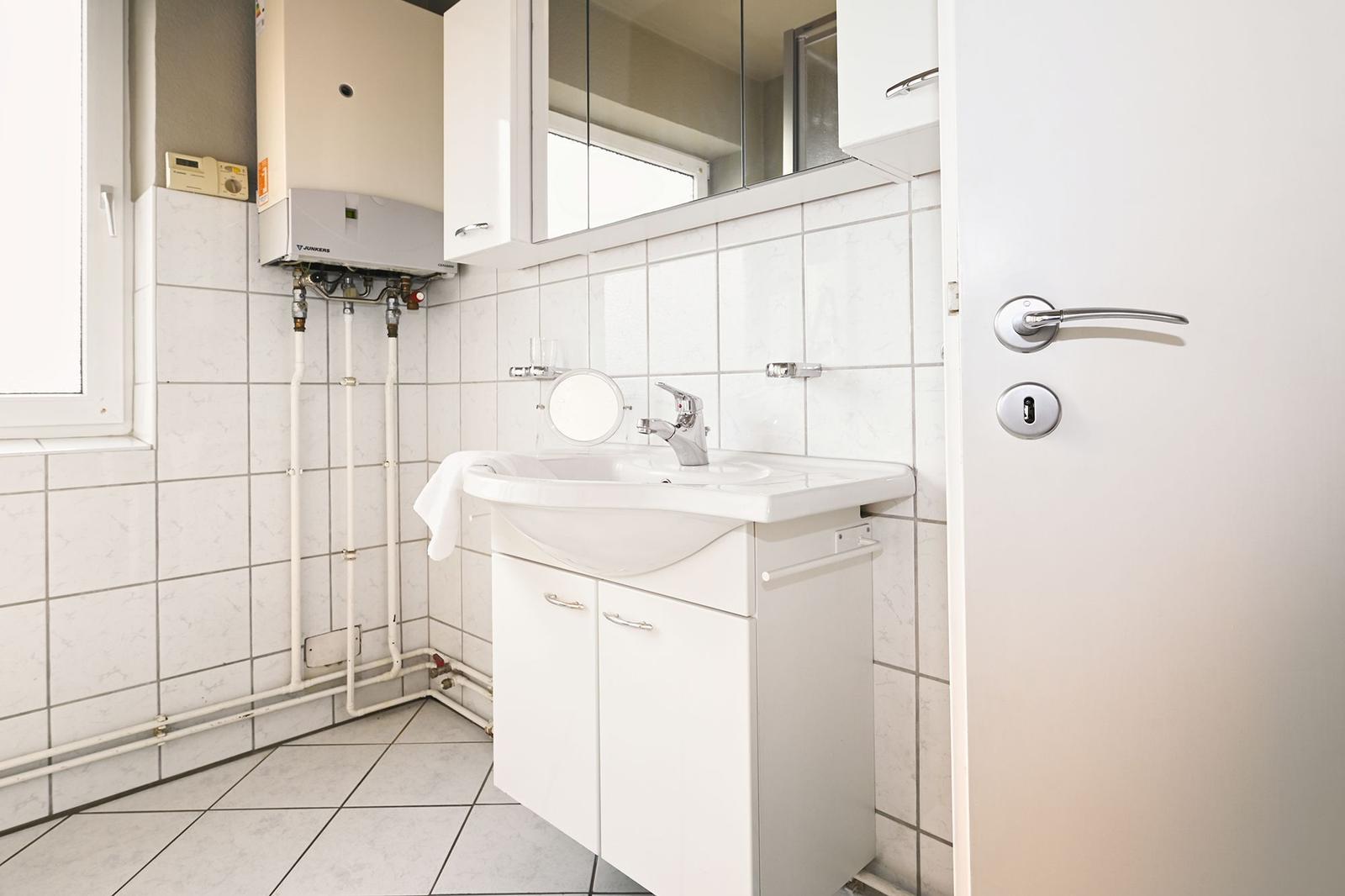 Badezimmer mit Waschbecken, Spiegel und Heizung.
