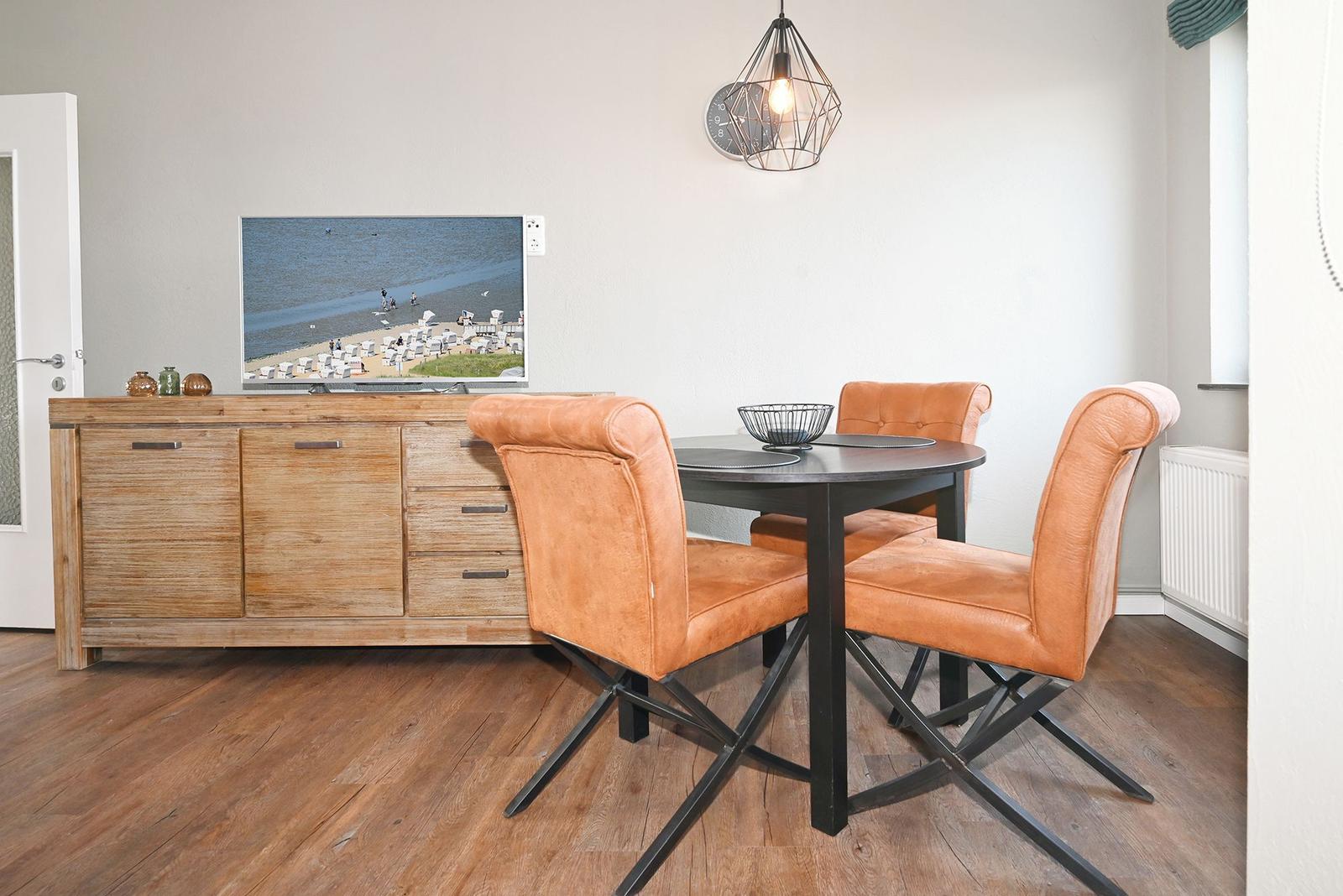 Esszimmer mit runden Tisch, drei orangefarbenen Stühlen und Holzsideboard.