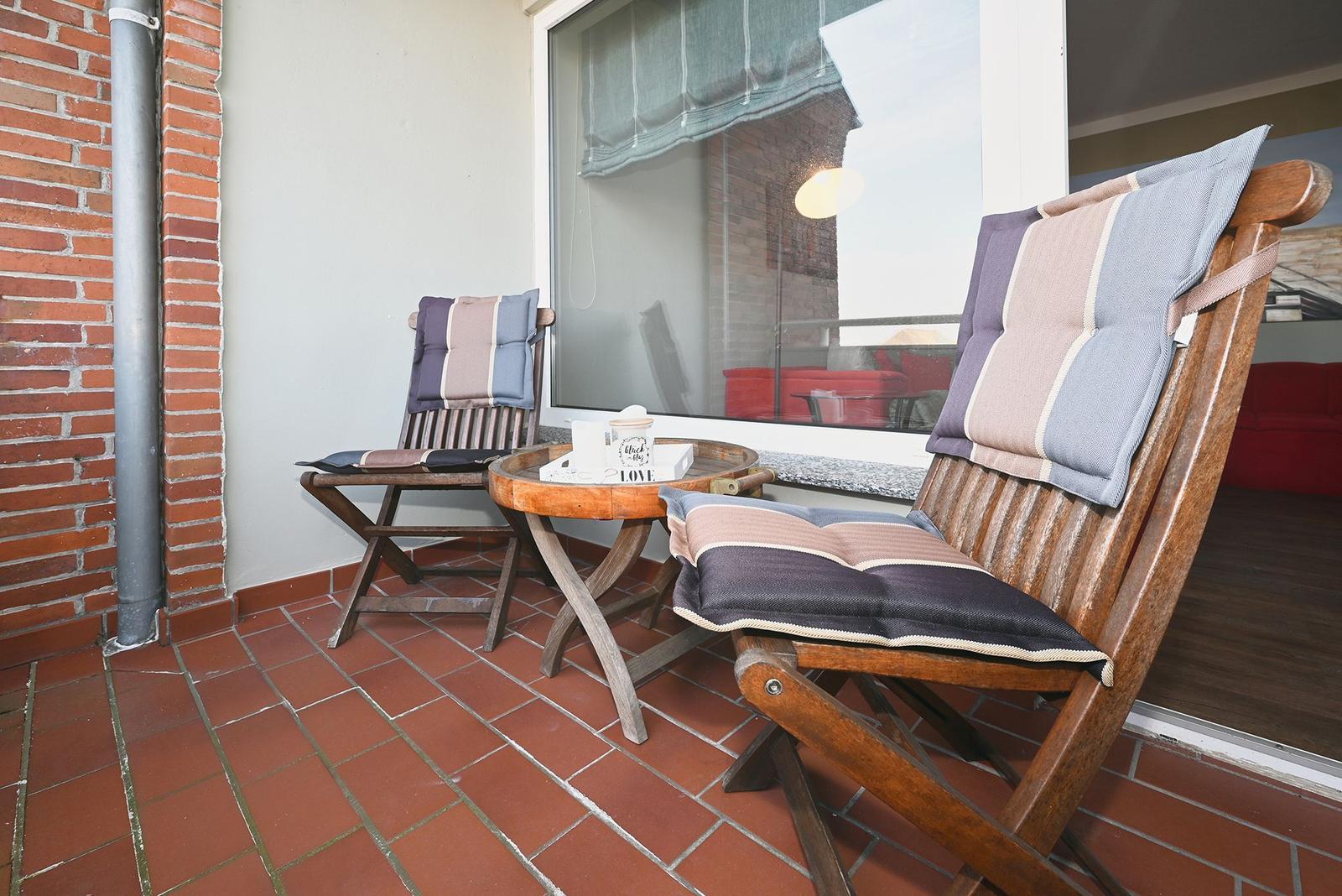 Terrasse mit zwei Holzstühlen, Tisch und rotem Fliesenboden.