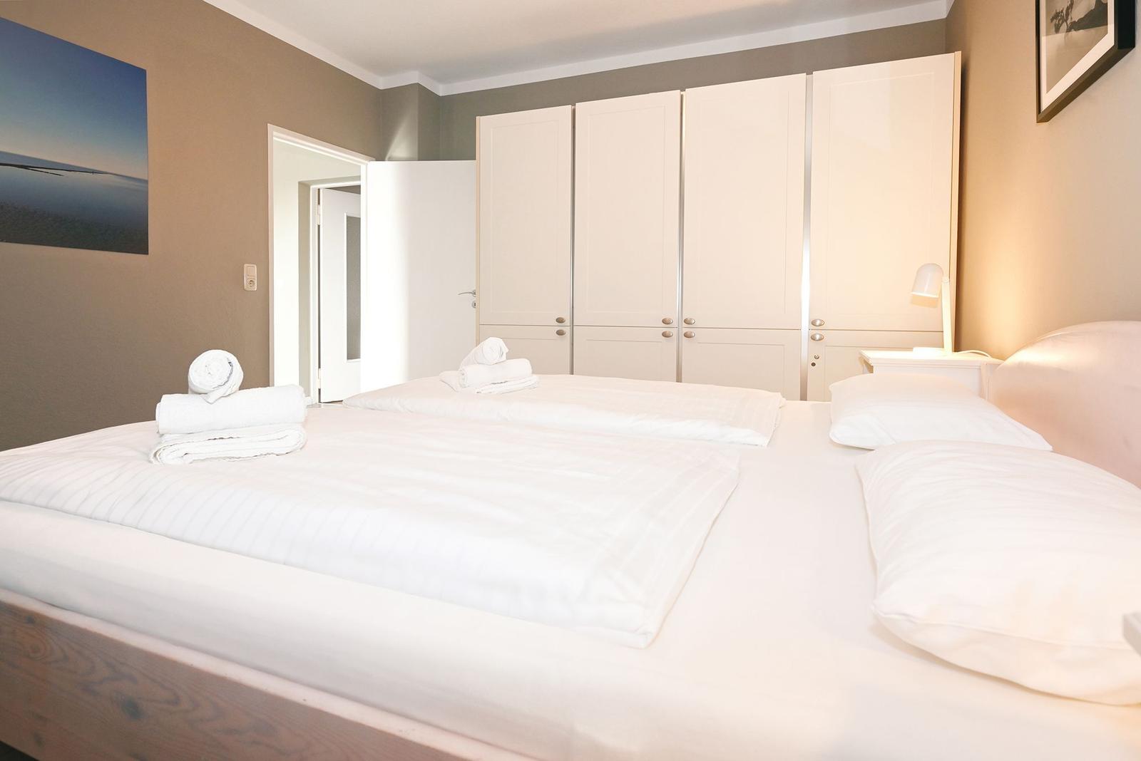 Schlafzimmer mit Doppelbett, weißen Bettwäsche und Kleiderschrank.