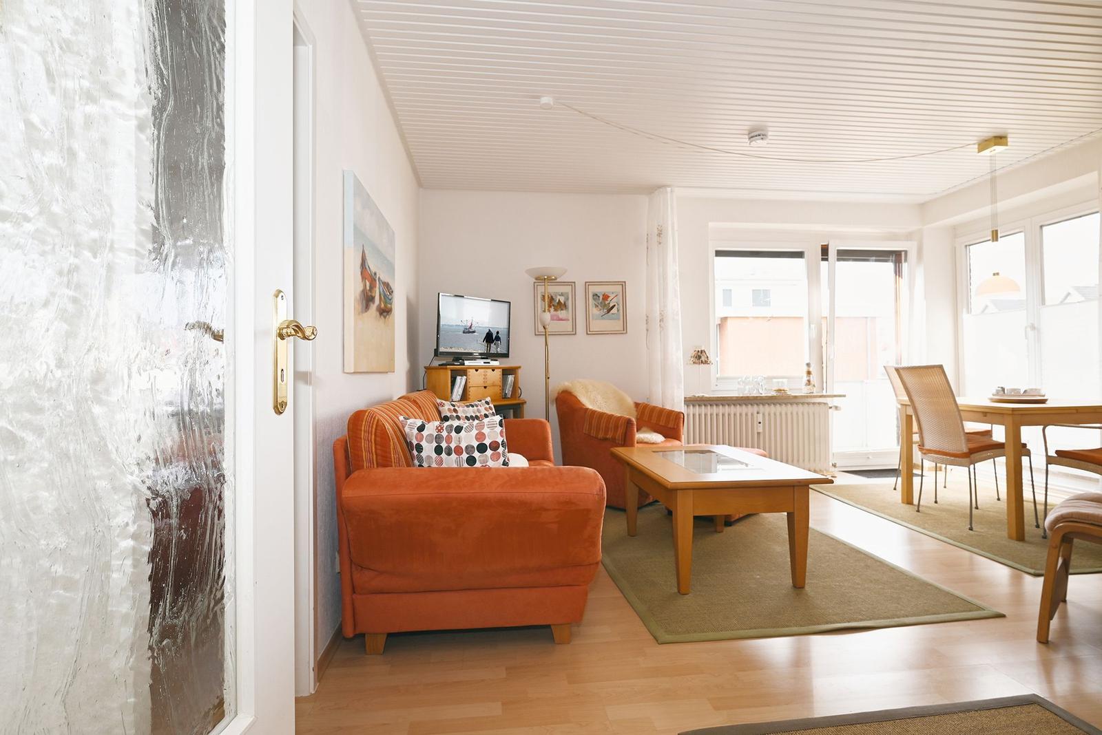 Wohn- und Essbereich mit orangefarbenem Sofa, Holztisch und Fenster.