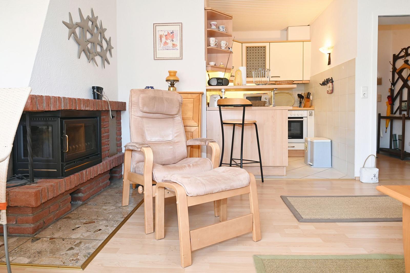 Wohnzimmer mit Sessel, Kamin und Blick in die Küche.