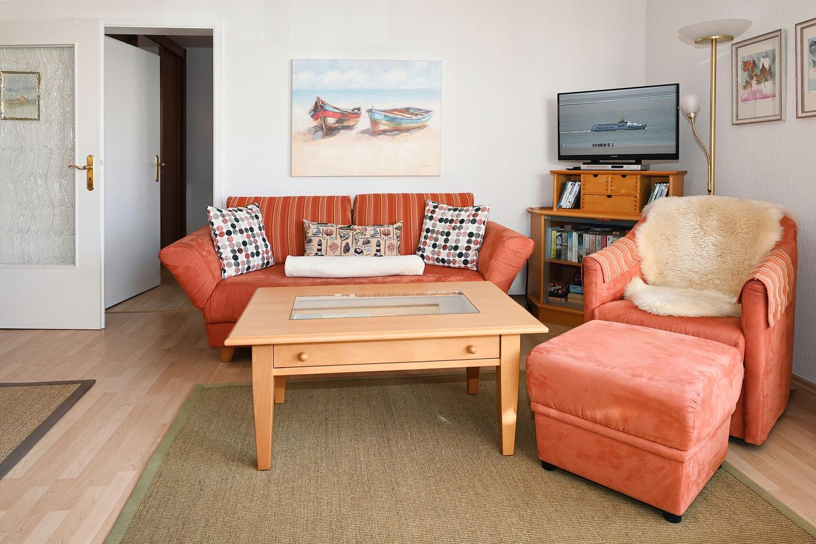Wohnzimmer mit Sofa, Sessel und Fernseher. Wandbild mit Booten.