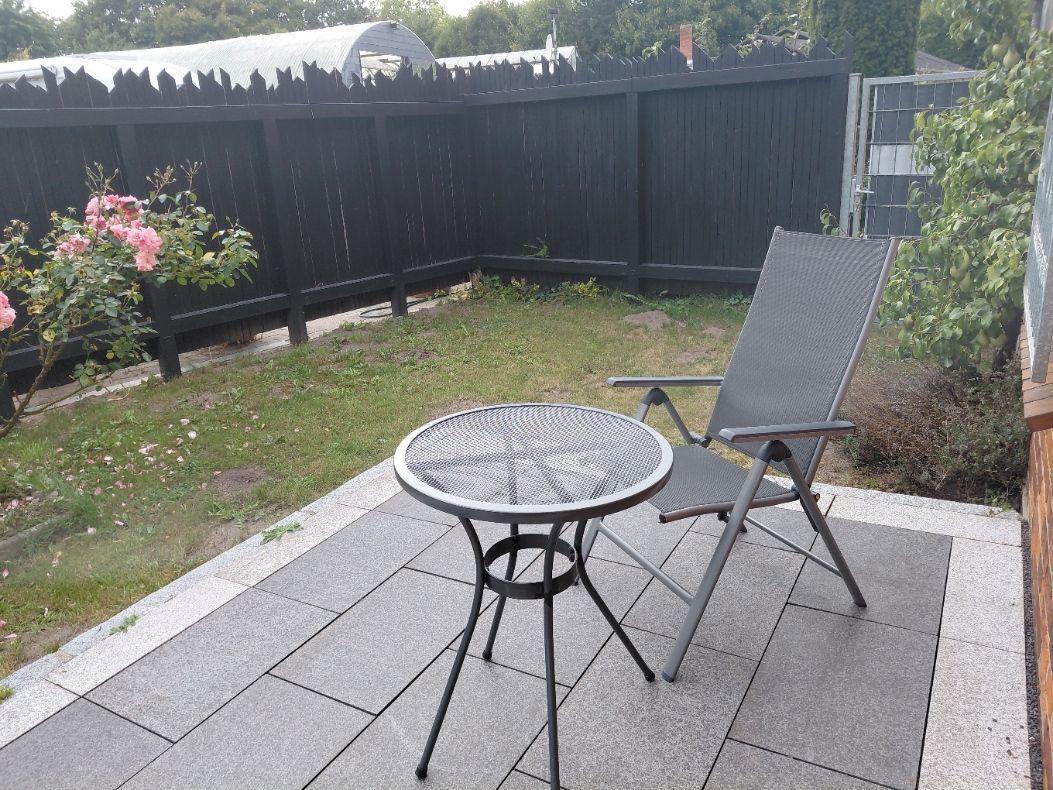 Terrasse mit Tisch und Stuhl, umgeben von Gras und Rosen.