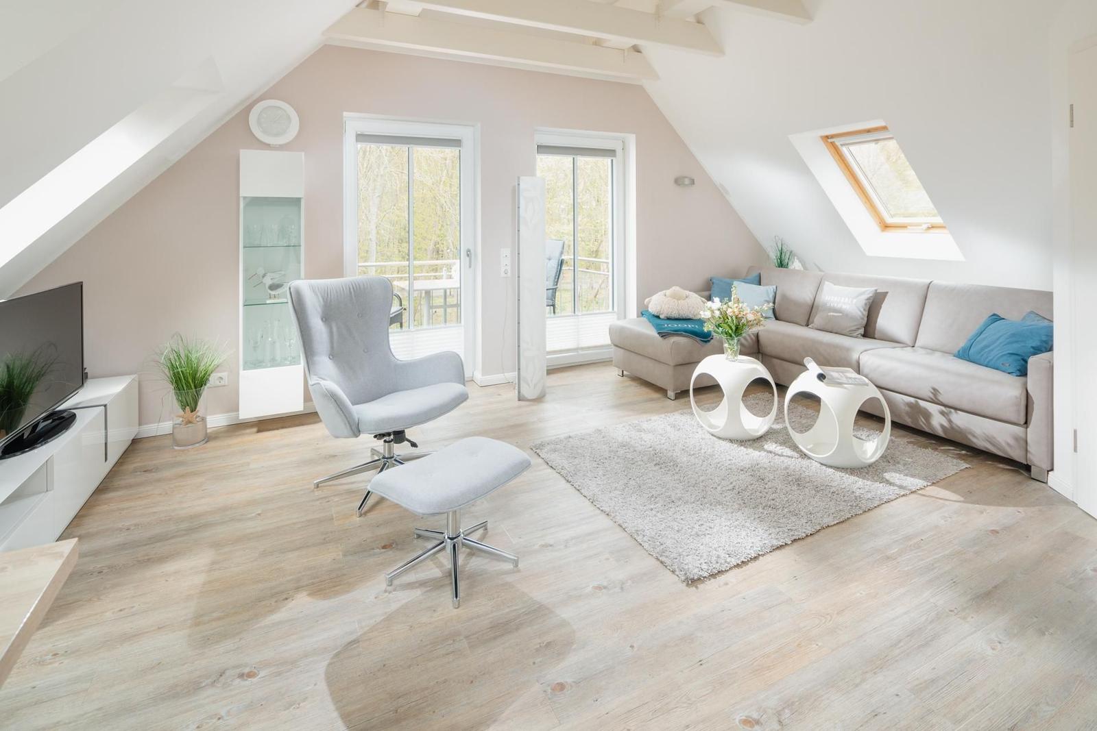 Wohnzimmer mit Sofa, Sessel und Fenstern. Holzboden und Dachschrägen.