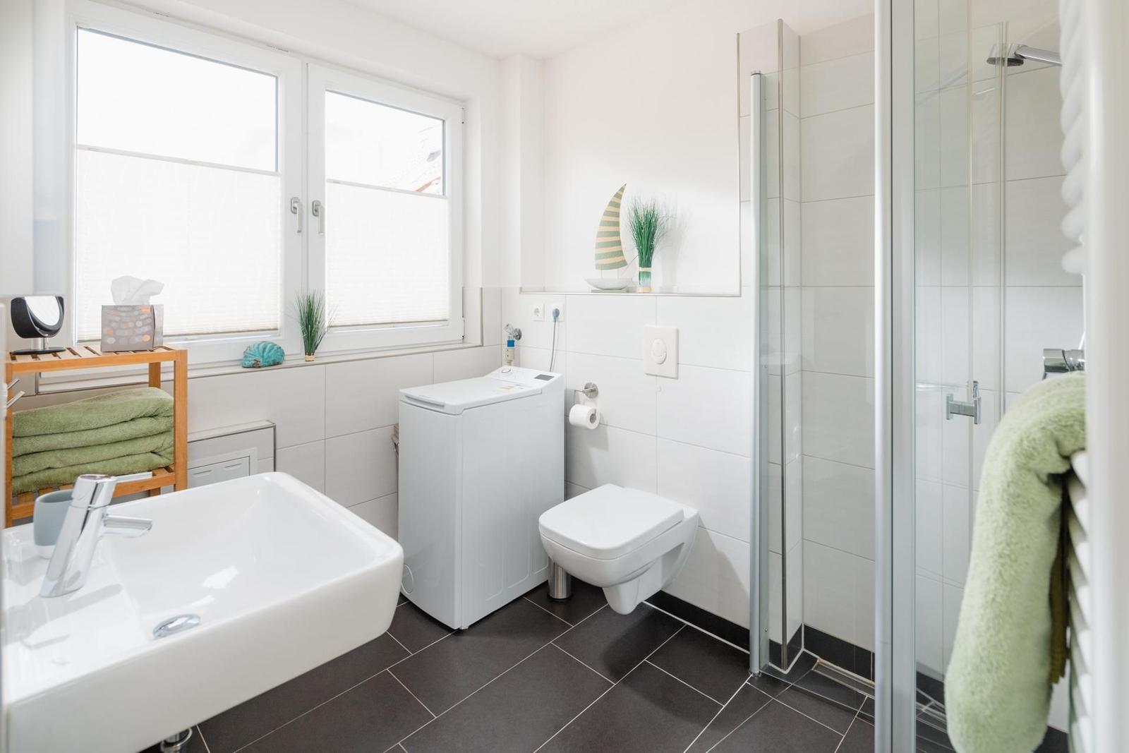 Badezimmer mit Dusche, Toilette, Waschmaschine und Fenster