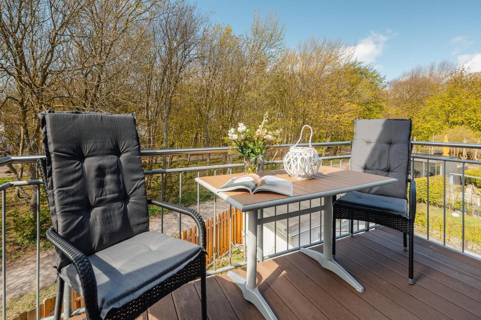 Terrasse mit Tisch und zwei Stühlen, Blick auf Wald und Himmel.