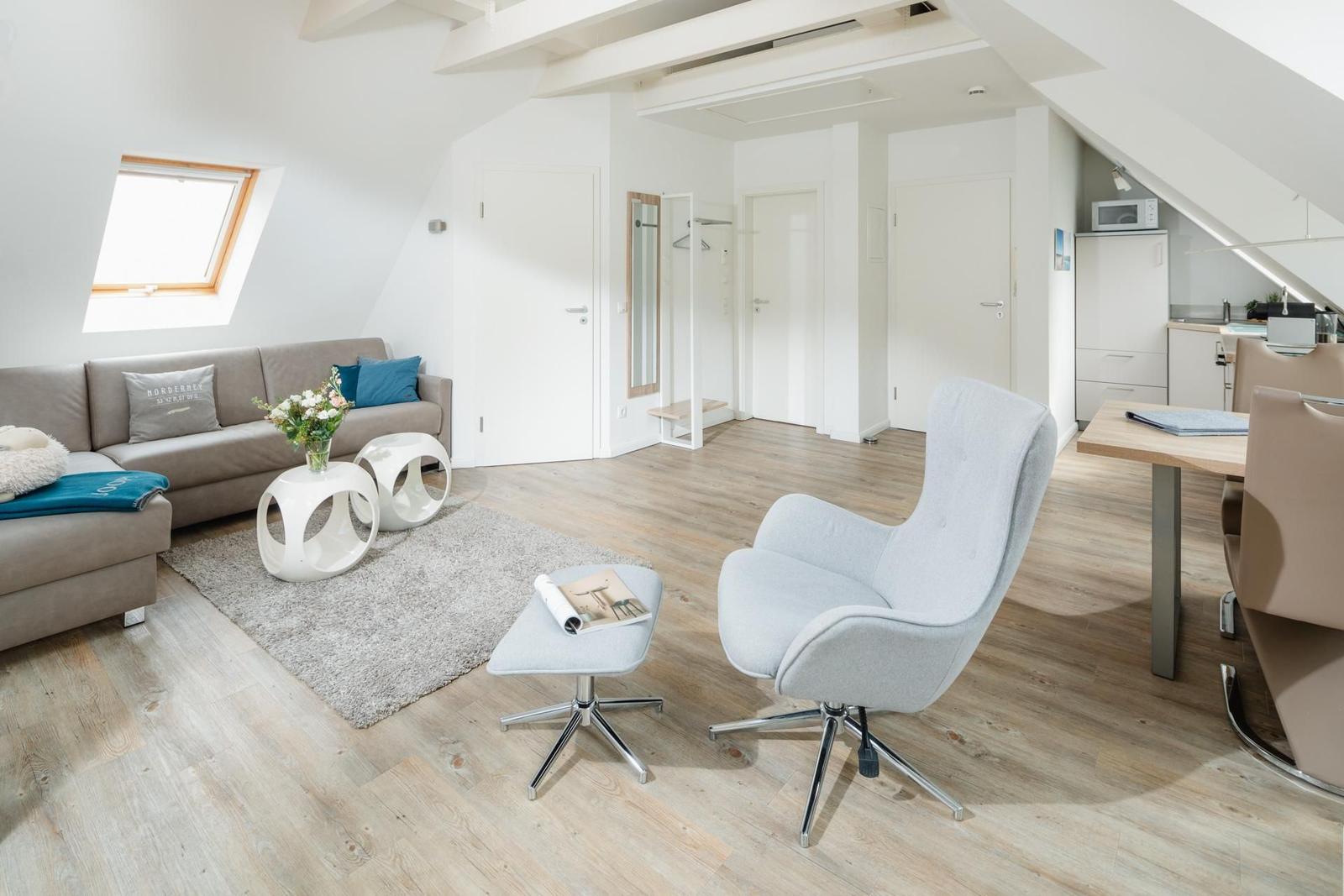 Wohnbereich mit Sofa, Sessel und Essbereich unter Dachschrägen.